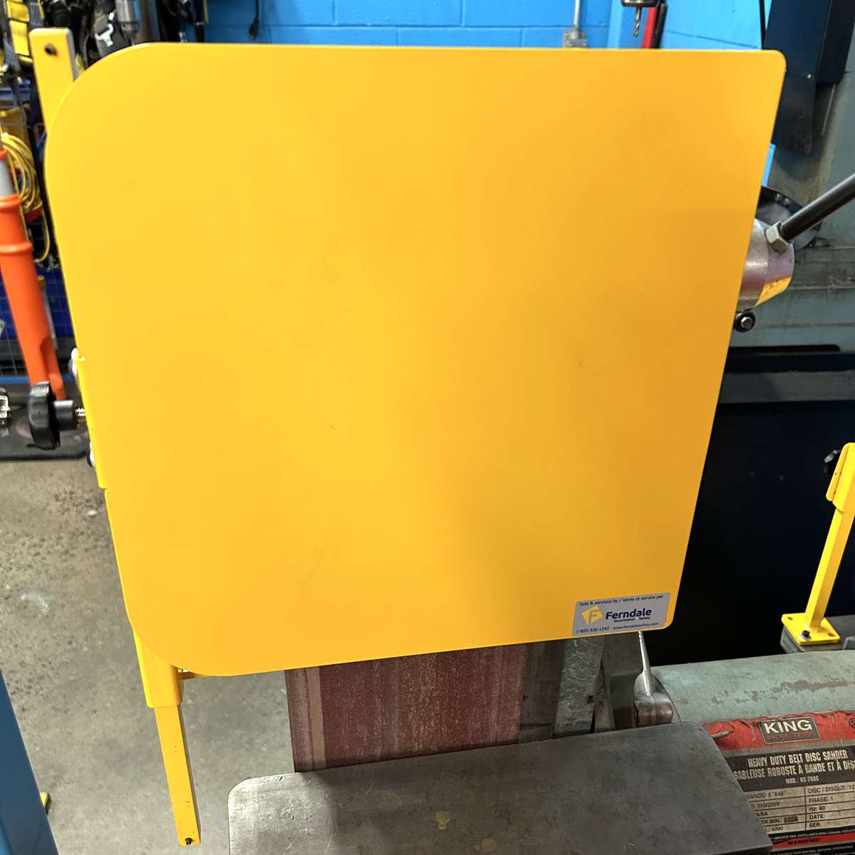A photo of an adjustable safety guard over top of a belt sander, protecting workers from abrasive material.