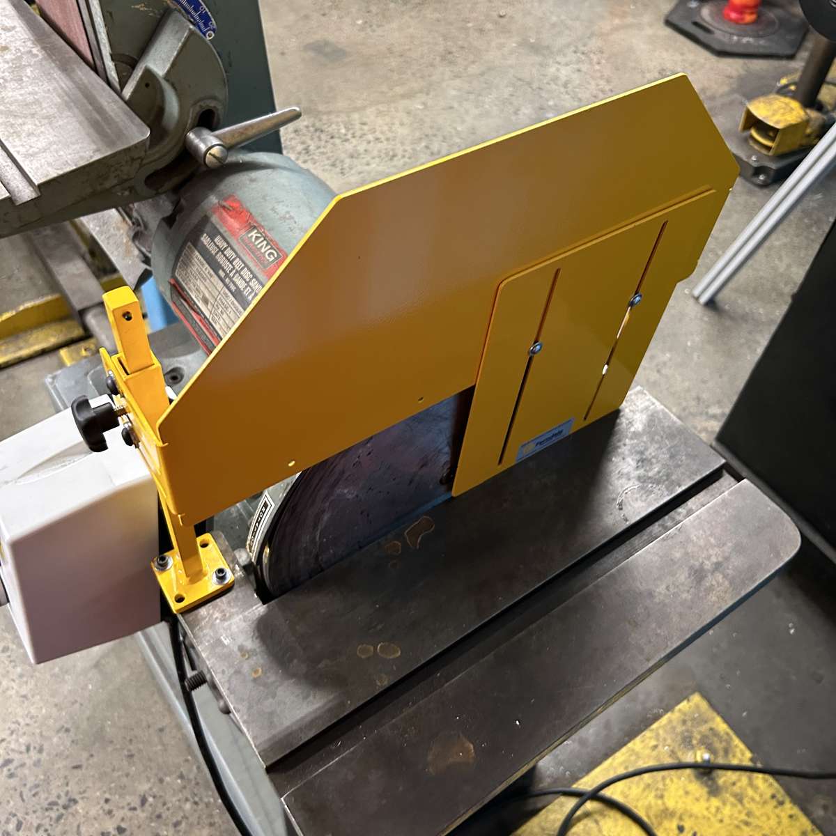 A top-view of an adjustable disk sander safety guard installed on a sanding machine.