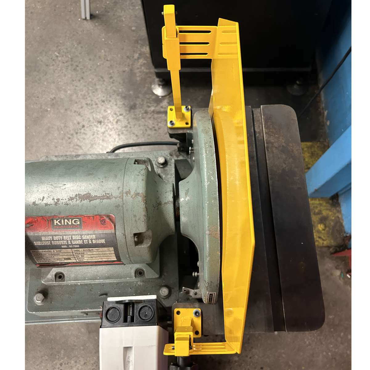 A top-view of an adjustable disk sander safety guard installed on a sanding machine.