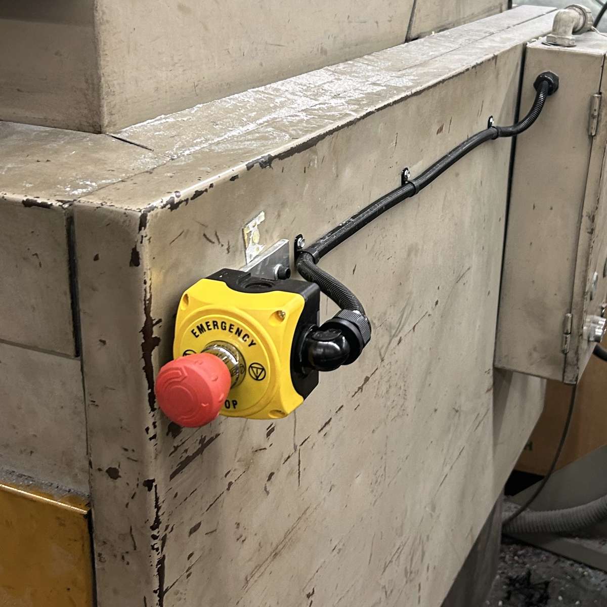 An image of an emergency stop button inside a yellow enclosure that is installed on the side of a machine. The red twist-release button on the yellow background of the enclosure is a well known indicator of an emergency stop button.