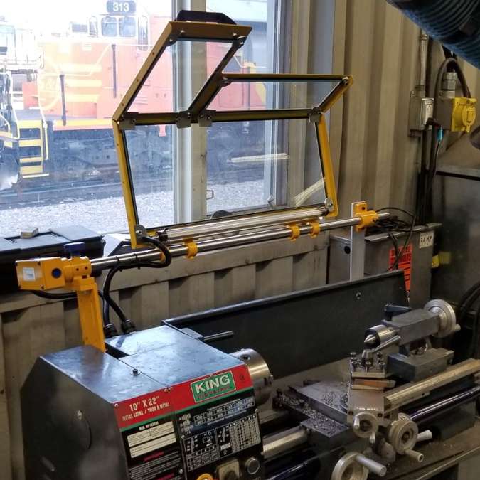 A safety guard installed on a King Industrial lathe with a train seen in the background through an outdoor window.